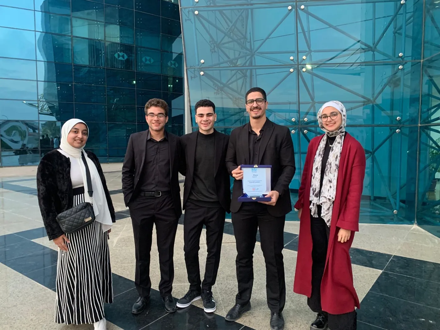 Five people standing with a certificate outside a glass building